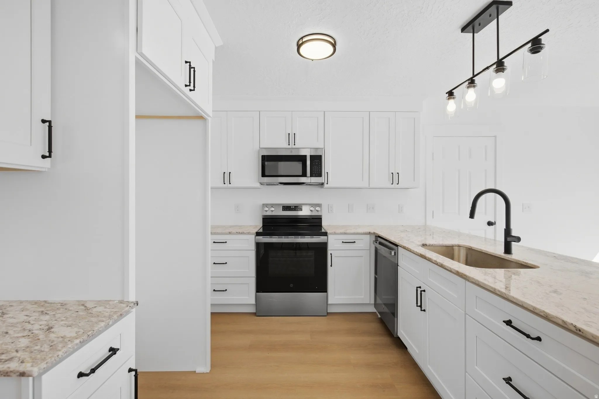 White cabinetry with matte black hardware, stainless steel appliances, light-toned countertops, a stainless steel sink with a matte black gooseneck faucet, and wood-finish flooring