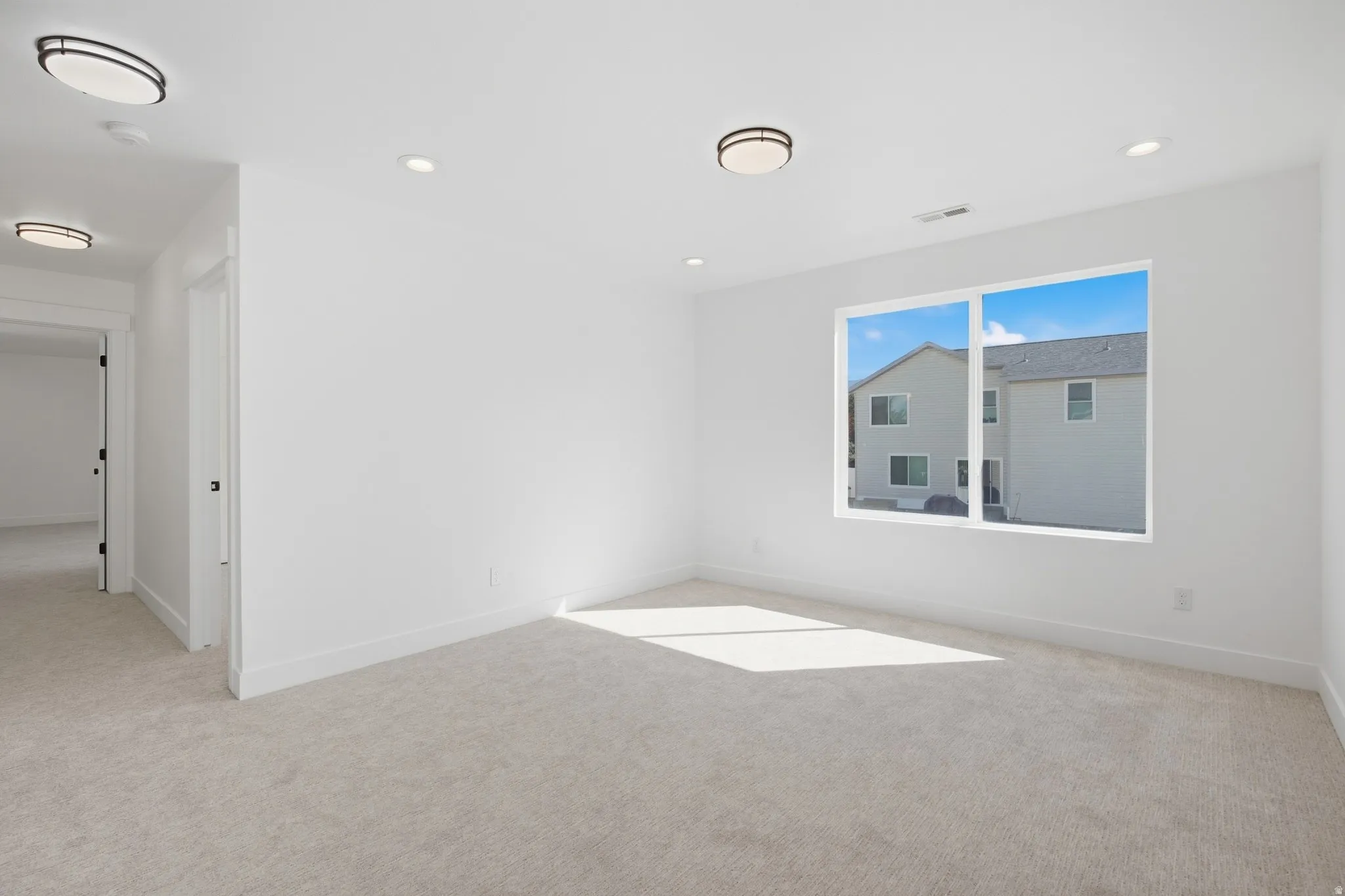 White walls, light-colored carpeting, recessed lighting, flush-mount light fixtures, and a large window