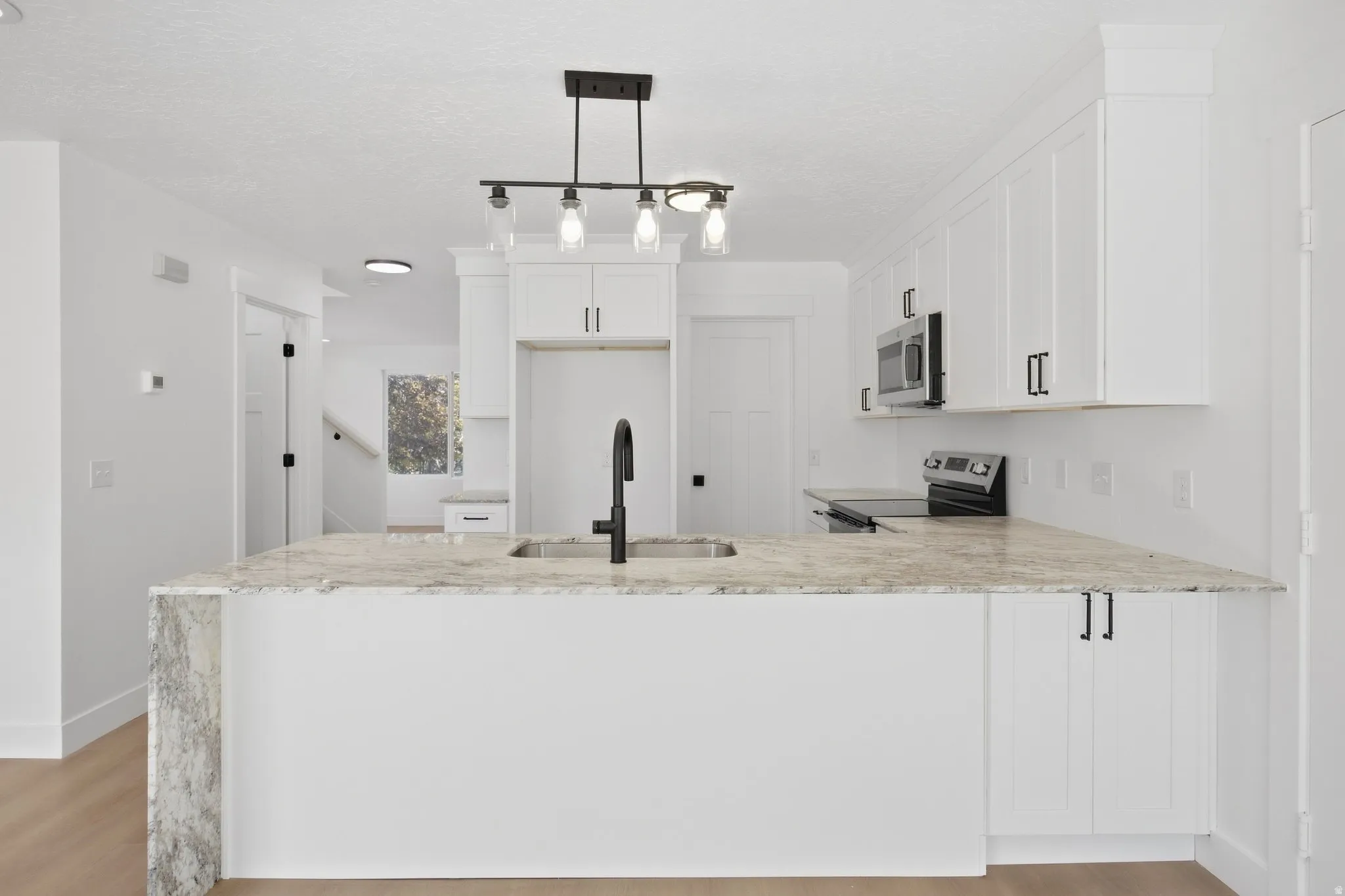 Kitchen island with a built-in sink and faucet, integrated stainless steel appliances, white shaker-style cabinetry with dark hardware, and recessed lighting