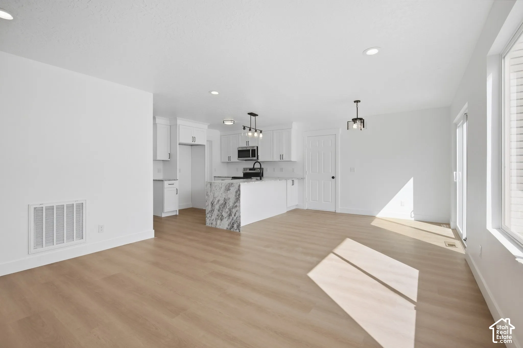 Open-concept main living area with wood-finish flooring, recessed lighting, and a kitchen island featuring a waterfall-edge countertop