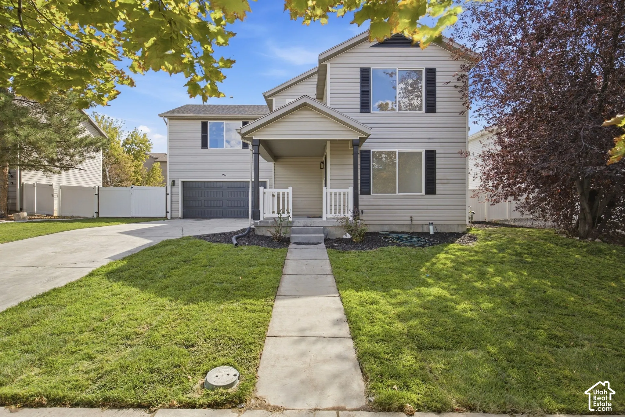 Two-story residence featuring light-toned siding, a covered entry porch, and an attached garage with a dark door