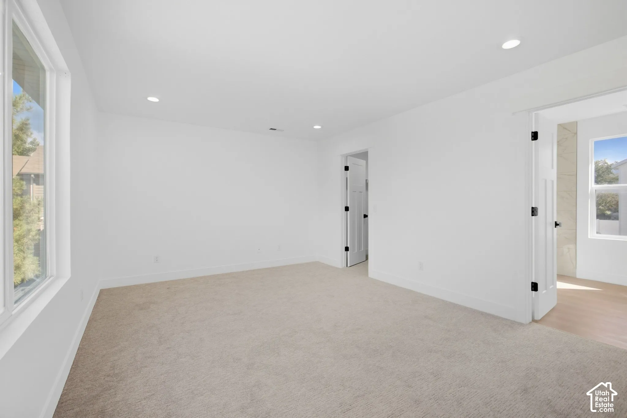 Recessed lighting, white walls, light-colored carpeting, white trim, and a white interior door with black hardware