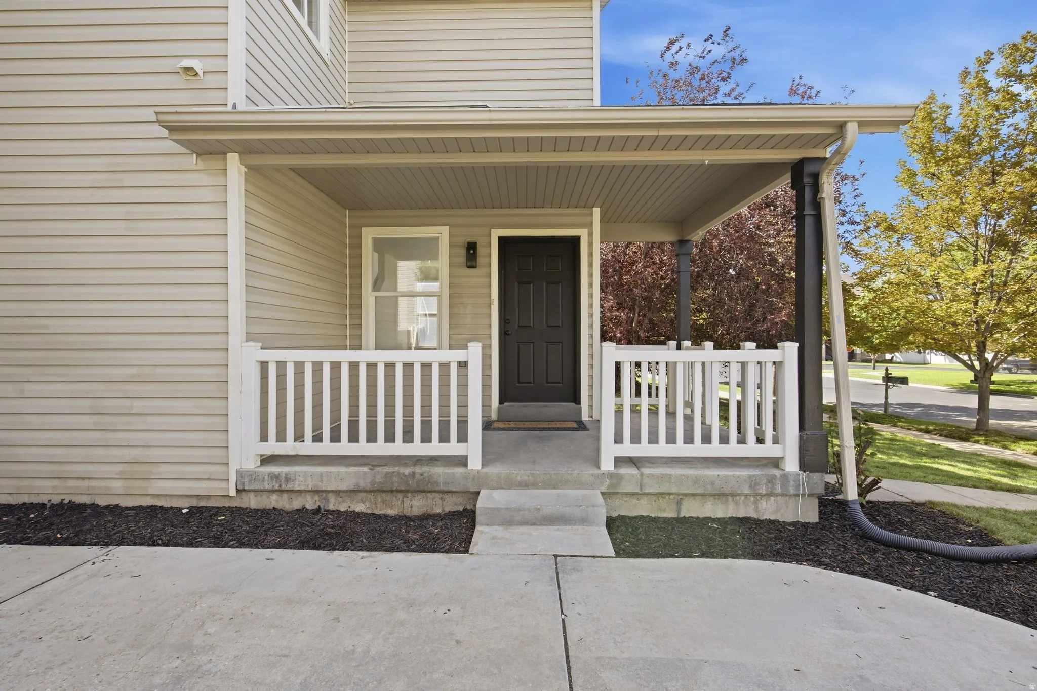 Covered front porch with white railings, a black entry door, and light-colored siding
