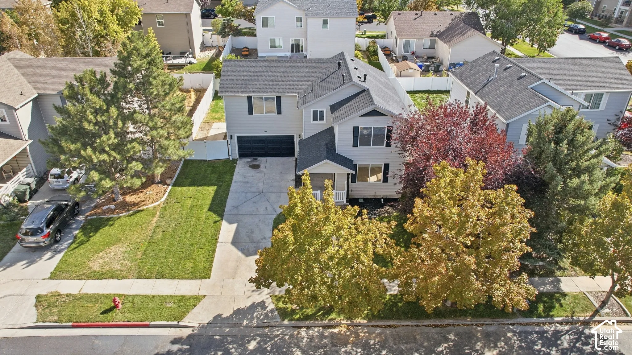 Two-story residential architecture with an attached garage, featuring a concrete driveway and mature trees
