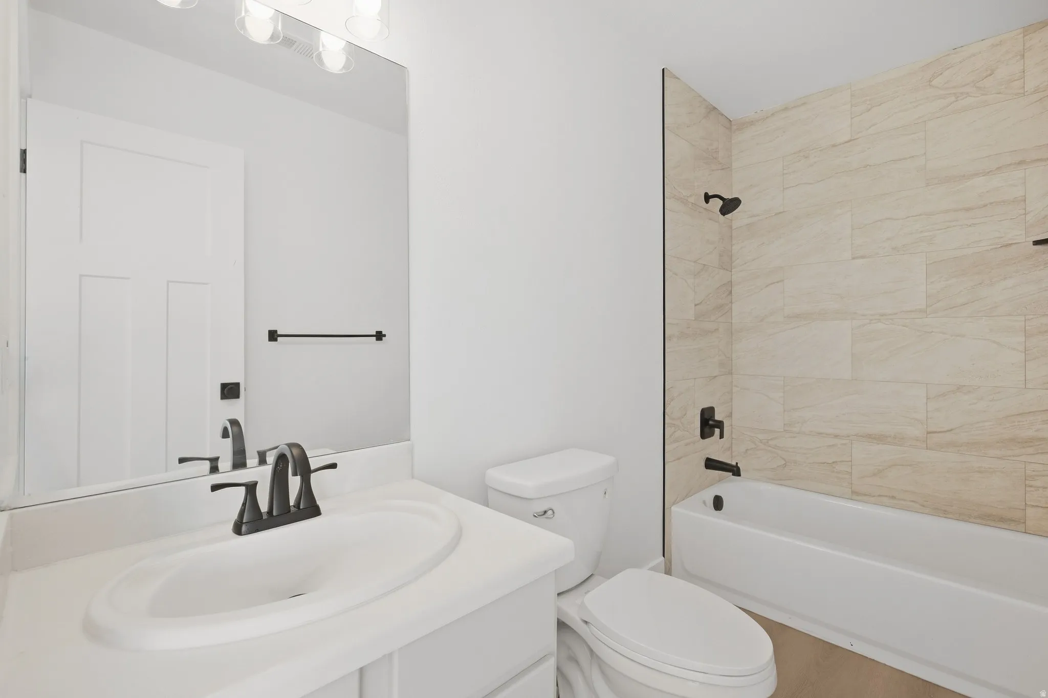 Contemporary bathroom featuring a vanity with an integrated sink, matte black fixtures, a rectangular mirror, a bathtub with a tiled shower surround, and a wall-mounted light fixture