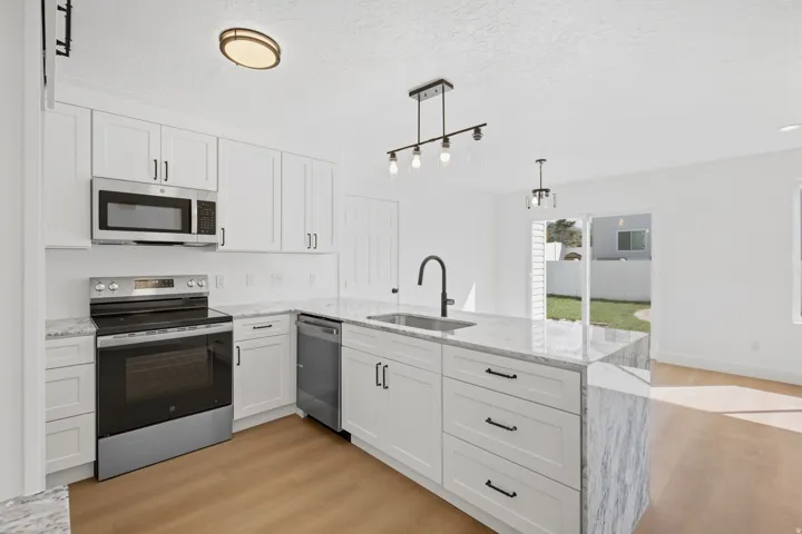 Modern kitchen featuring white shaker cabinetry, stainless steel appliances, and light-toned wood-finish flooring