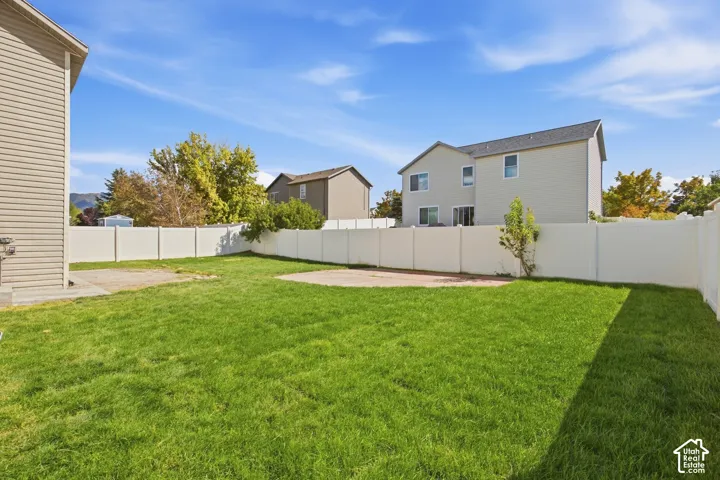 Expansive grassy yard with a white privacy fence and a concrete patio