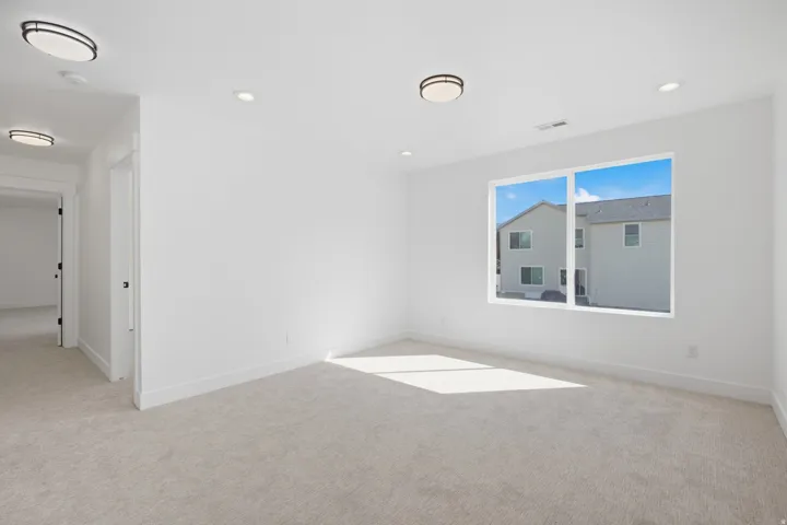 White walls, light-colored carpeting, recessed lighting, flush-mount light fixtures, and a large window