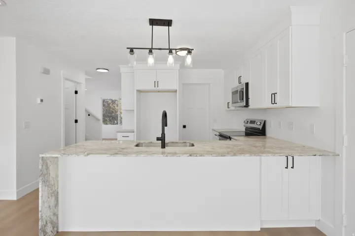 Kitchen island with a built-in sink and faucet, integrated stainless steel appliances, white shaker-style cabinetry with dark hardware, and recessed lighting