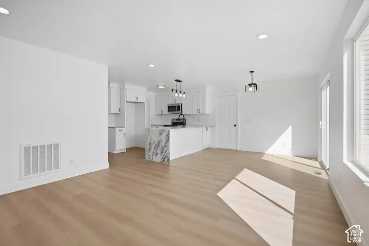 Open-concept main living area with wood-finish flooring, recessed lighting, and a kitchen island featuring a waterfall-edge countertop