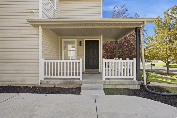 Covered front porch with white railings, a black entry door, and light-colored siding