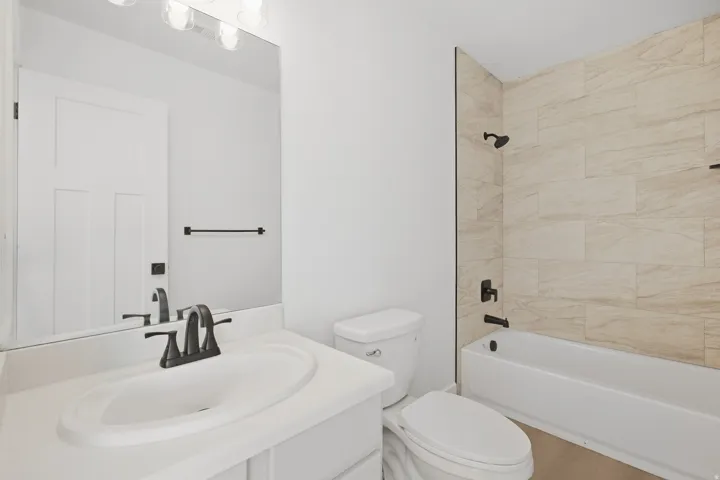 Contemporary bathroom featuring a vanity with an integrated sink, matte black fixtures, a rectangular mirror, a bathtub with a tiled shower surround, and a wall-mounted light fixture
