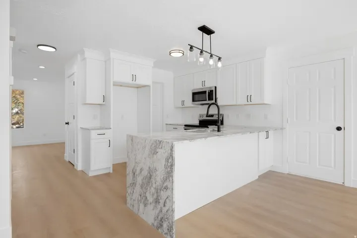 Kitchen featuring white cabinetry, a large center island with a waterfall countertop, stainless steel microwave, black faucet, and wood-finish flooring