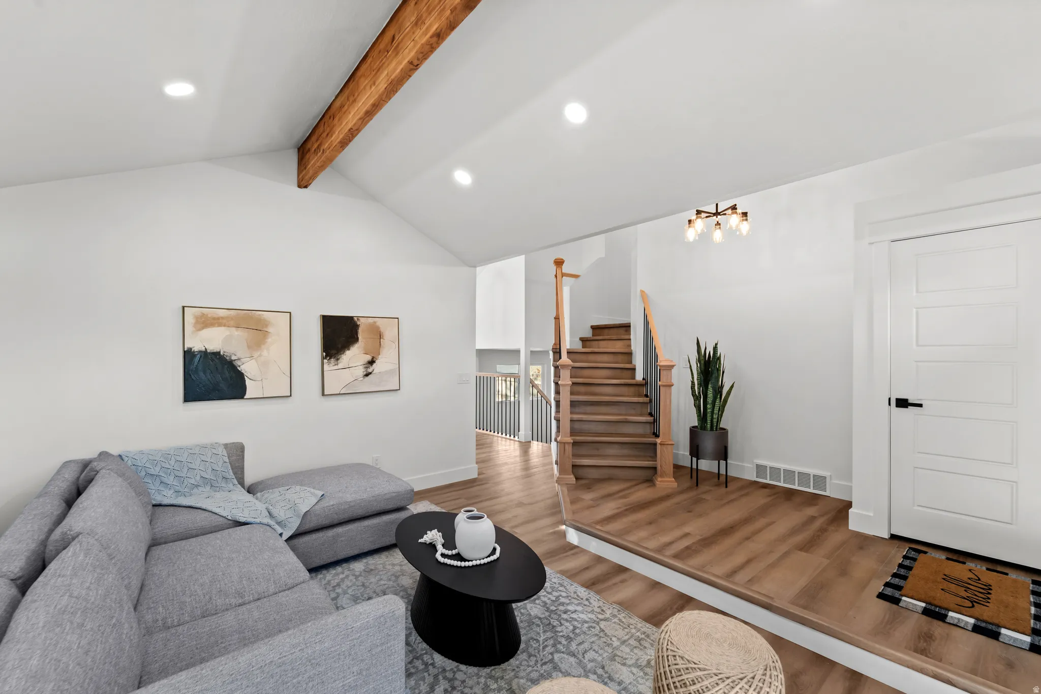 Vaulted ceiling with exposed wood beam, recessed lighting, wood-finish flooring, staircase with natural wood treads and railing, and a contemporary five-light chandelier