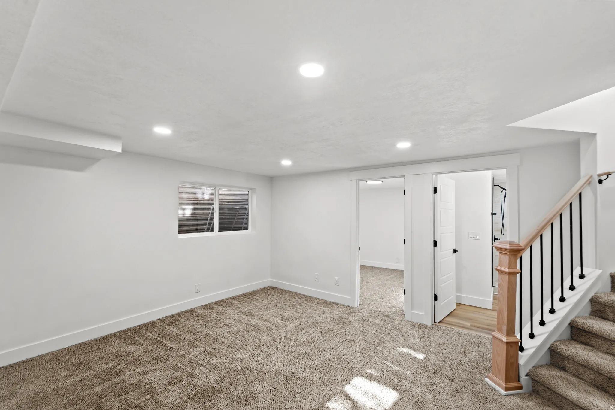 Recessed lighting throughout, plush carpet flooring, white trim, wood newel post with black iron balusters, and white paneled doors