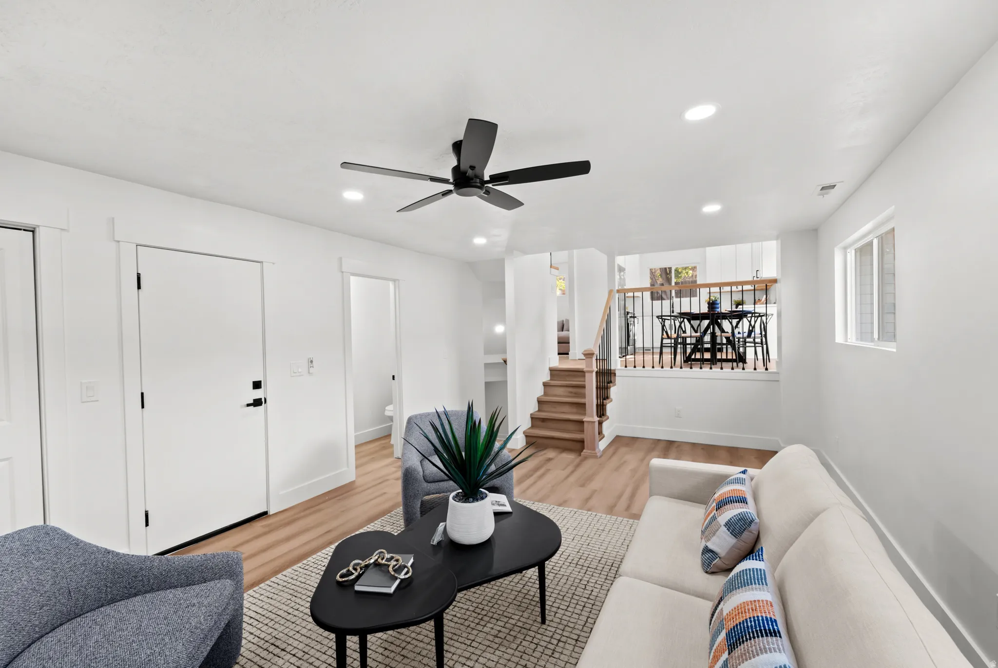 Recessed lighting, wood-finish flooring, a black ceiling fan, white interior doors with black hardware, and a staircase with a wood handrail and black metal balusters