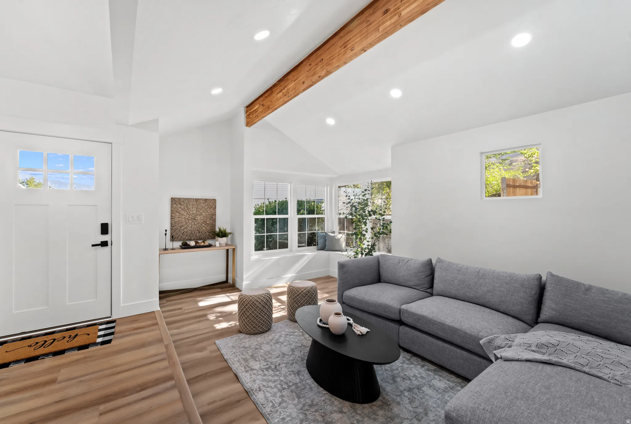 Vaulted ceiling with exposed wood beam, recessed lighting, wood-finish flooring, and multi-pane windows
