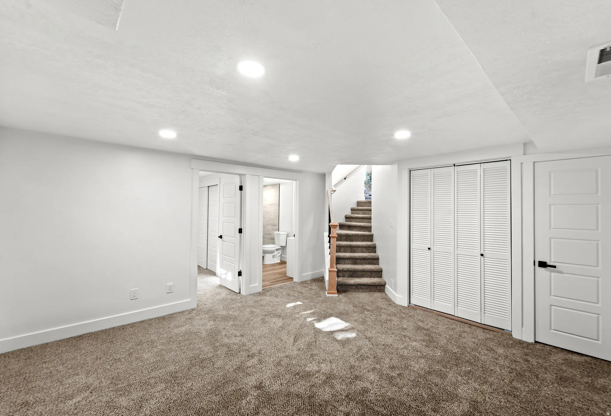 Carpeted room with recessed lighting, white trim, and a staircase featuring wood handrails