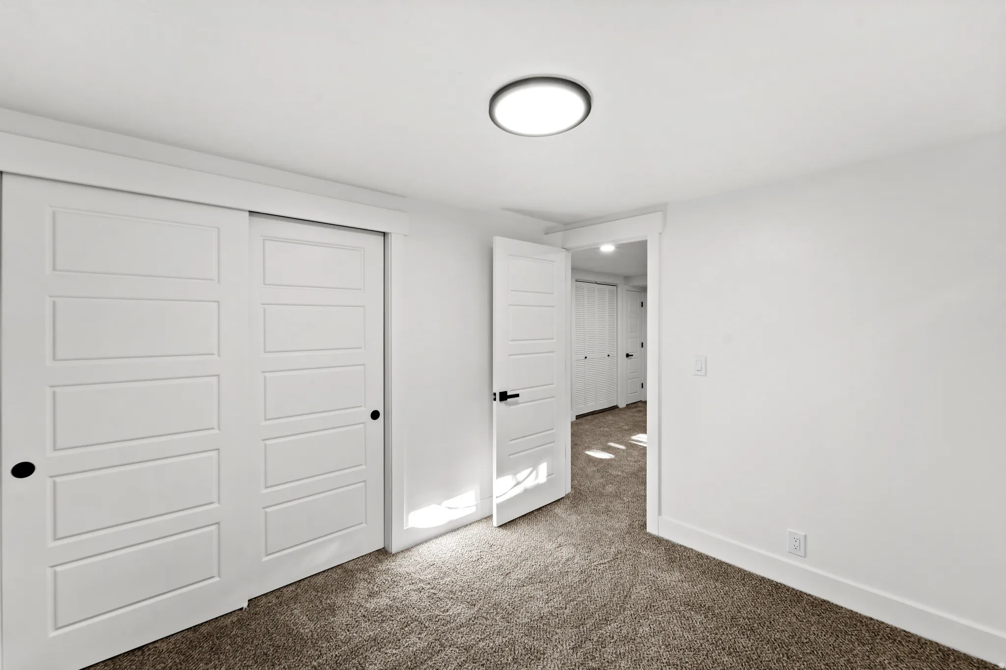 White paneled sliding closet doors, ceiling-mounted light fixture, and neutral carpet flooring