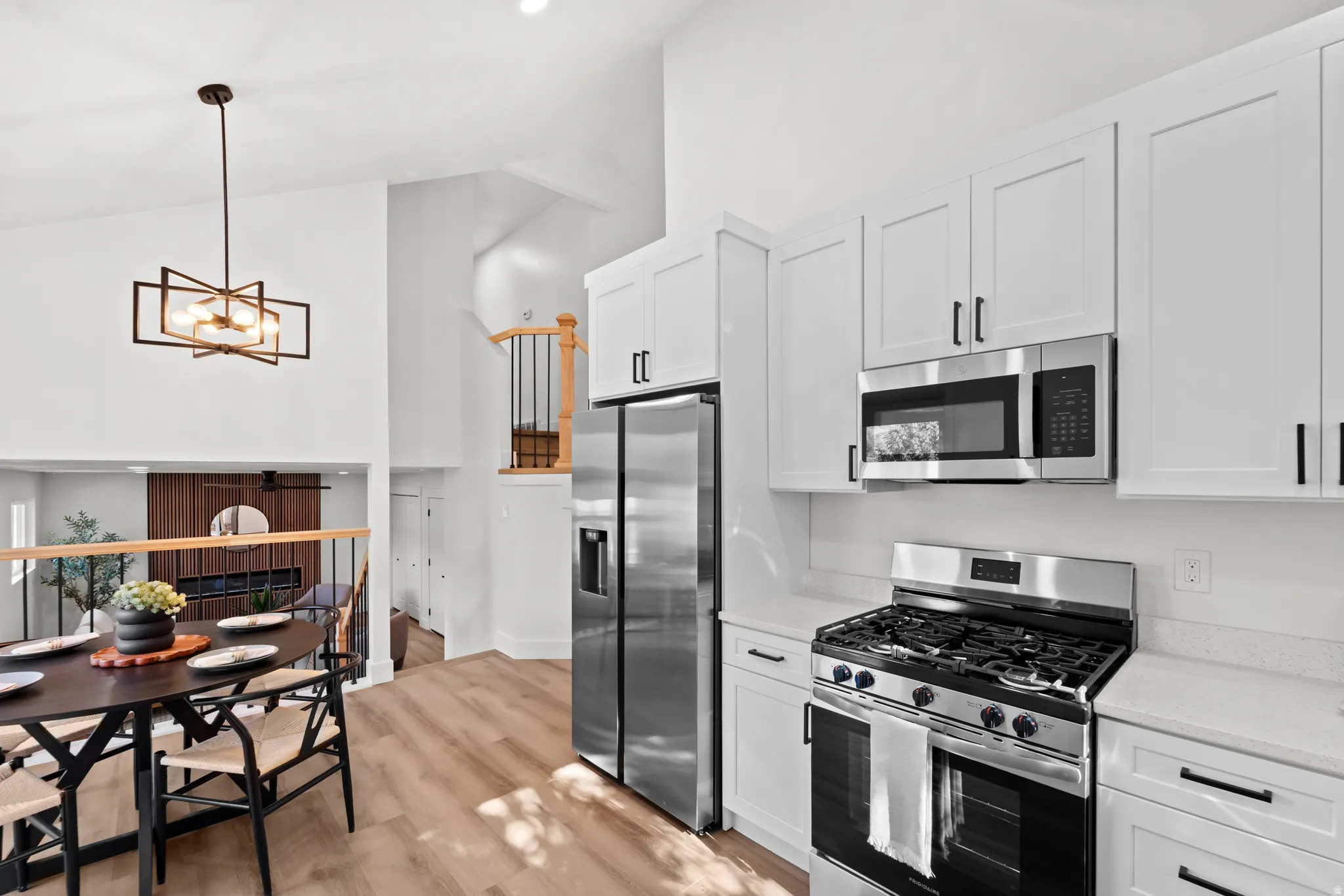 Modern kitchen with white cabinetry, stainless steel appliances, light-toned countertops, and wood-finish flooring