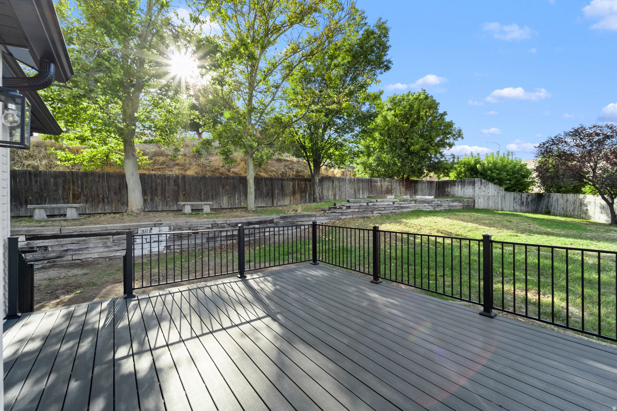 Spacious composite deck with black metal railing, featuring a terraced backyard with mature trees and a privacy fence