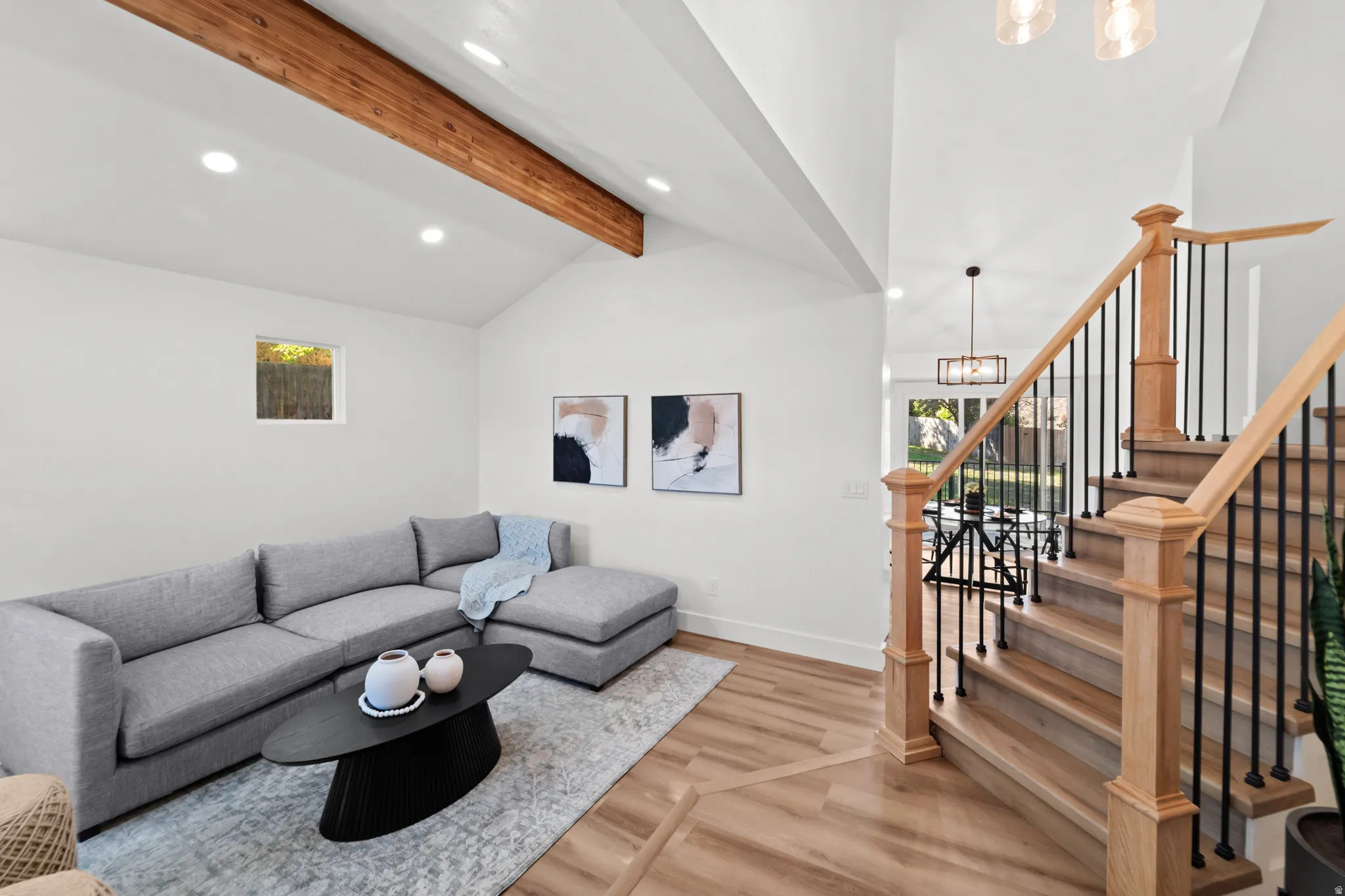 Vaulted ceiling with exposed wood beam, recessed lighting, wood-finish flooring, and a natural wood staircase with wrought iron balusters