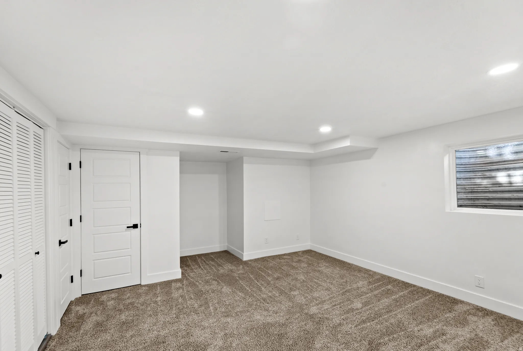 Recessed lighting, white trim, textured carpeting, panel doors with matte black hardware, and an egress window