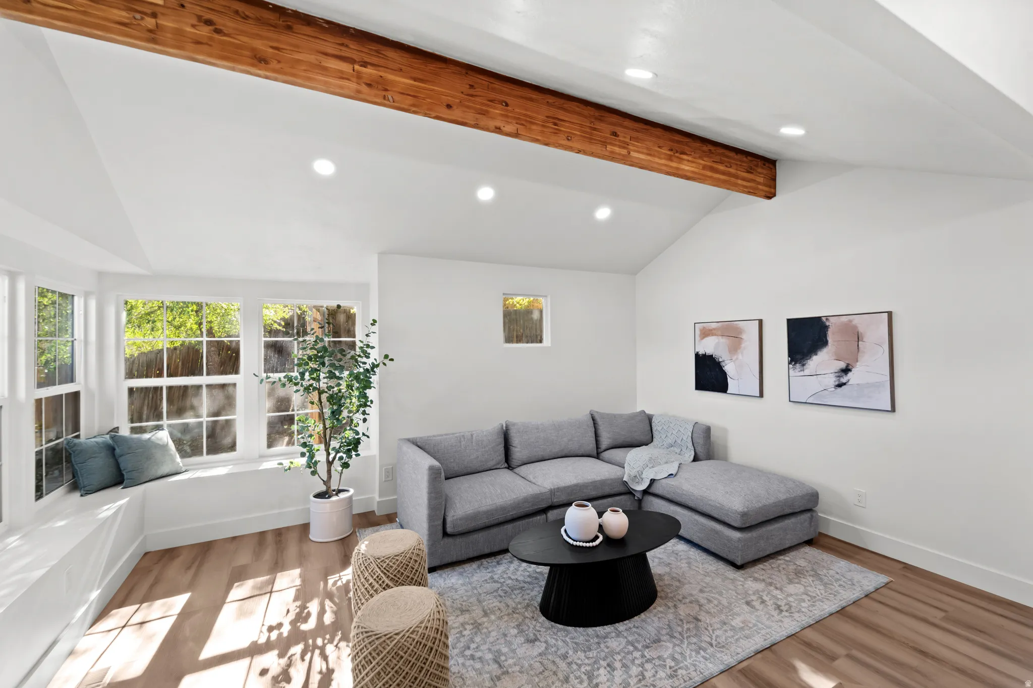 Vaulted ceiling with exposed wood beam, recessed lighting, expansive bay windows with integrated window seat, and wood-finish flooring