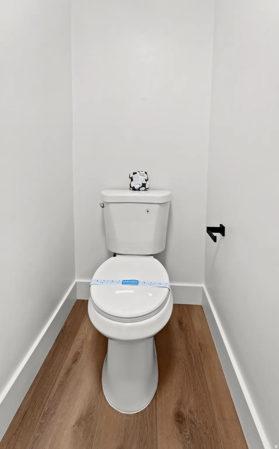 White toilet with wood-finish flooring and a matte black toilet paper holder