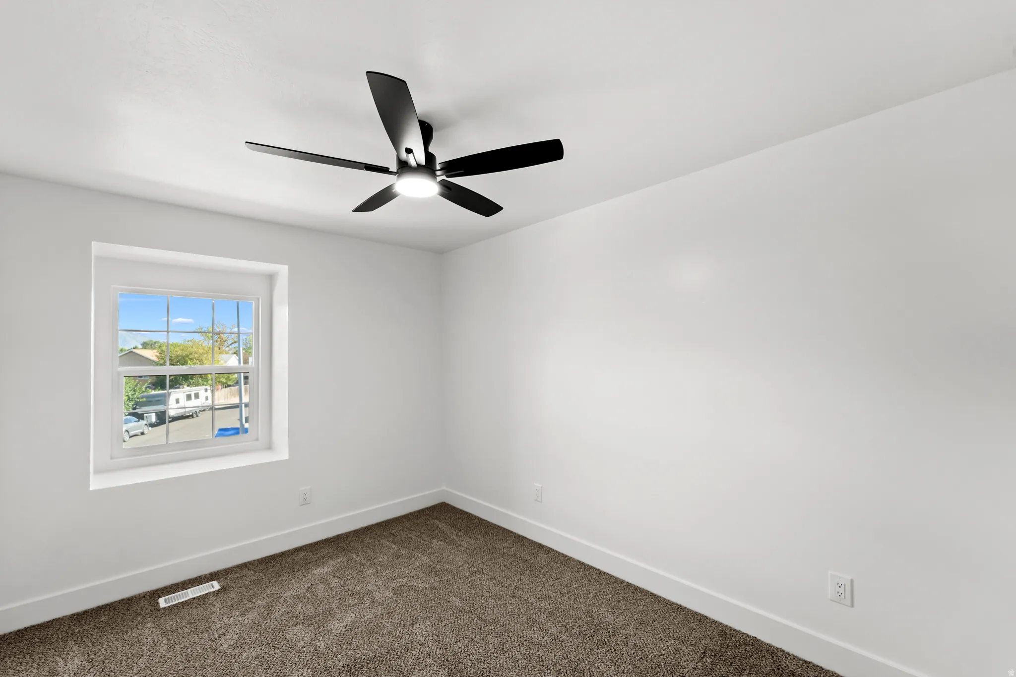 White painted walls, carpeted flooring, a black ceiling fan with integrated lighting, and a single window