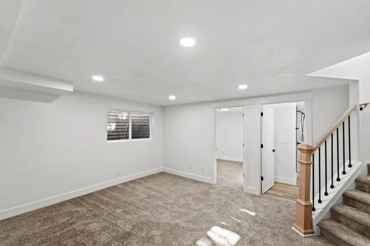 Recessed lighting throughout, plush carpet flooring, white trim, wood newel post with black iron balusters, and white paneled doors
