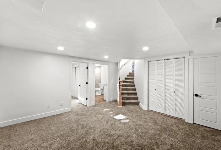 Carpeted room with recessed lighting, white trim, and a staircase featuring wood handrails