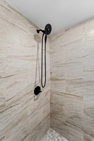 Shower enclosure featuring large format stone-look tile walls, matte black shower fixtures, and a pebble-style floor
