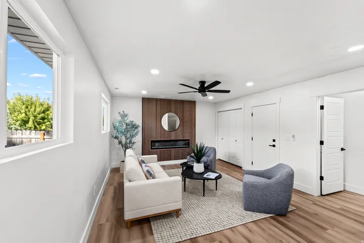 Spacious living area featuring wood-finish flooring, a contemporary ceiling fan, recessed lighting, a modern fireplace with a wood-paneled accent wall, and multiple windows