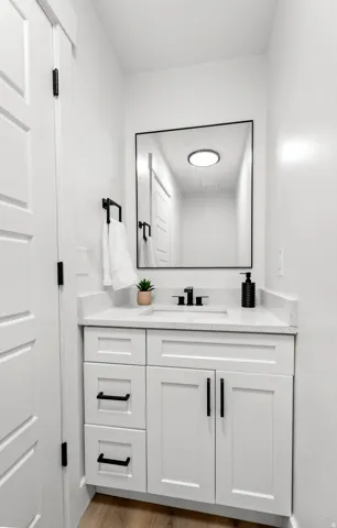 White shaker-style vanity with matte black hardware, integrated sink, and light-toned countertop