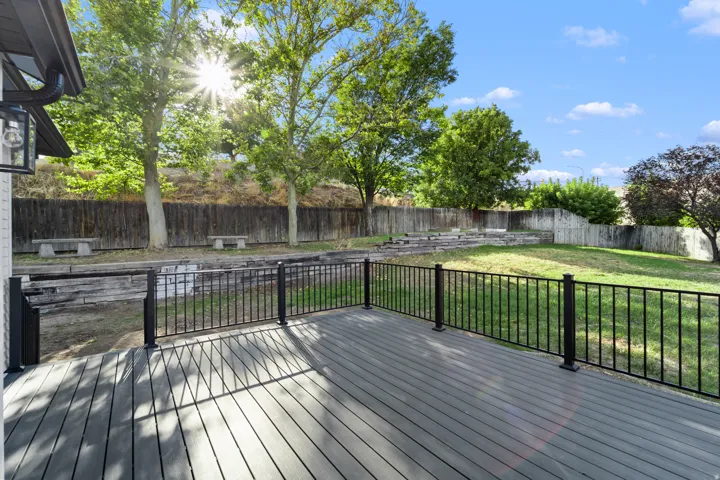 Spacious composite deck with black metal railing, featuring a terraced backyard with mature trees and a privacy fence