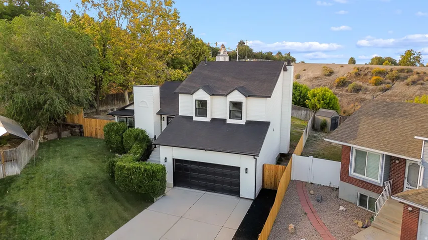White exterior with black trim, attached garage, concrete driveway, and mature landscaping