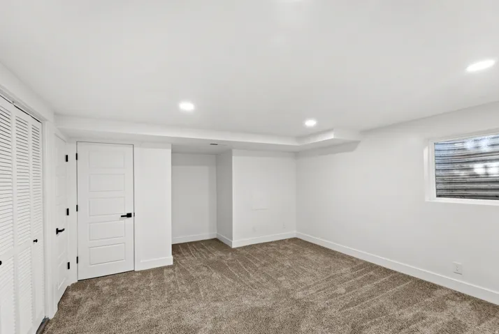 Recessed lighting, white trim, textured carpeting, panel doors with matte black hardware, and an egress window