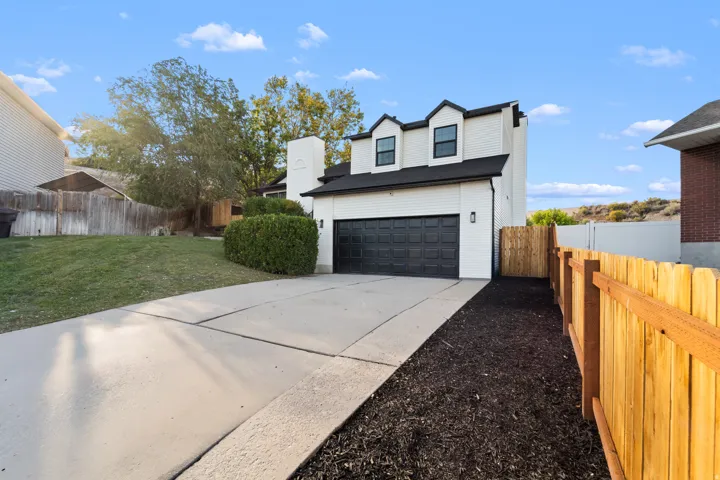 Exterior featuring white siding, black garage door, multiple dormer windows, and a newly installed wood fence