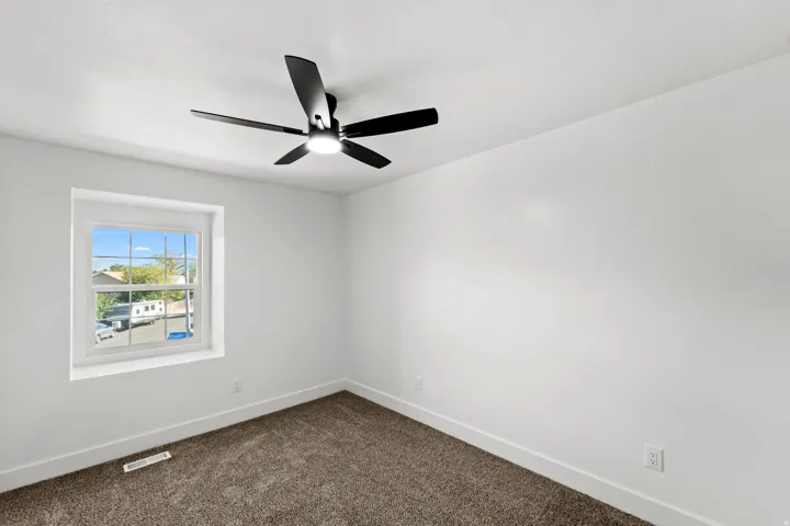 White painted walls, carpeted flooring, a black ceiling fan with integrated lighting, and a single window