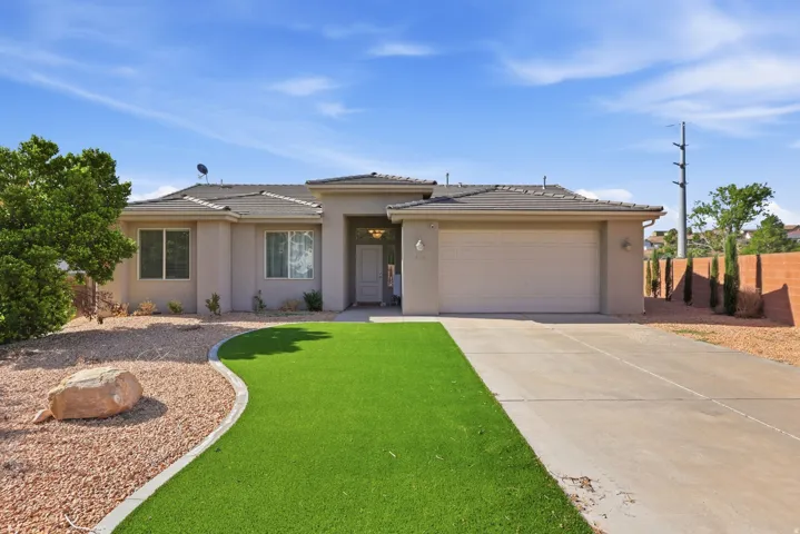 Stucco exterior with a tile roof, an integrated two-car garage, a concrete driveway, and low-maintenance landscaping featuring artificial turf and decorative rock