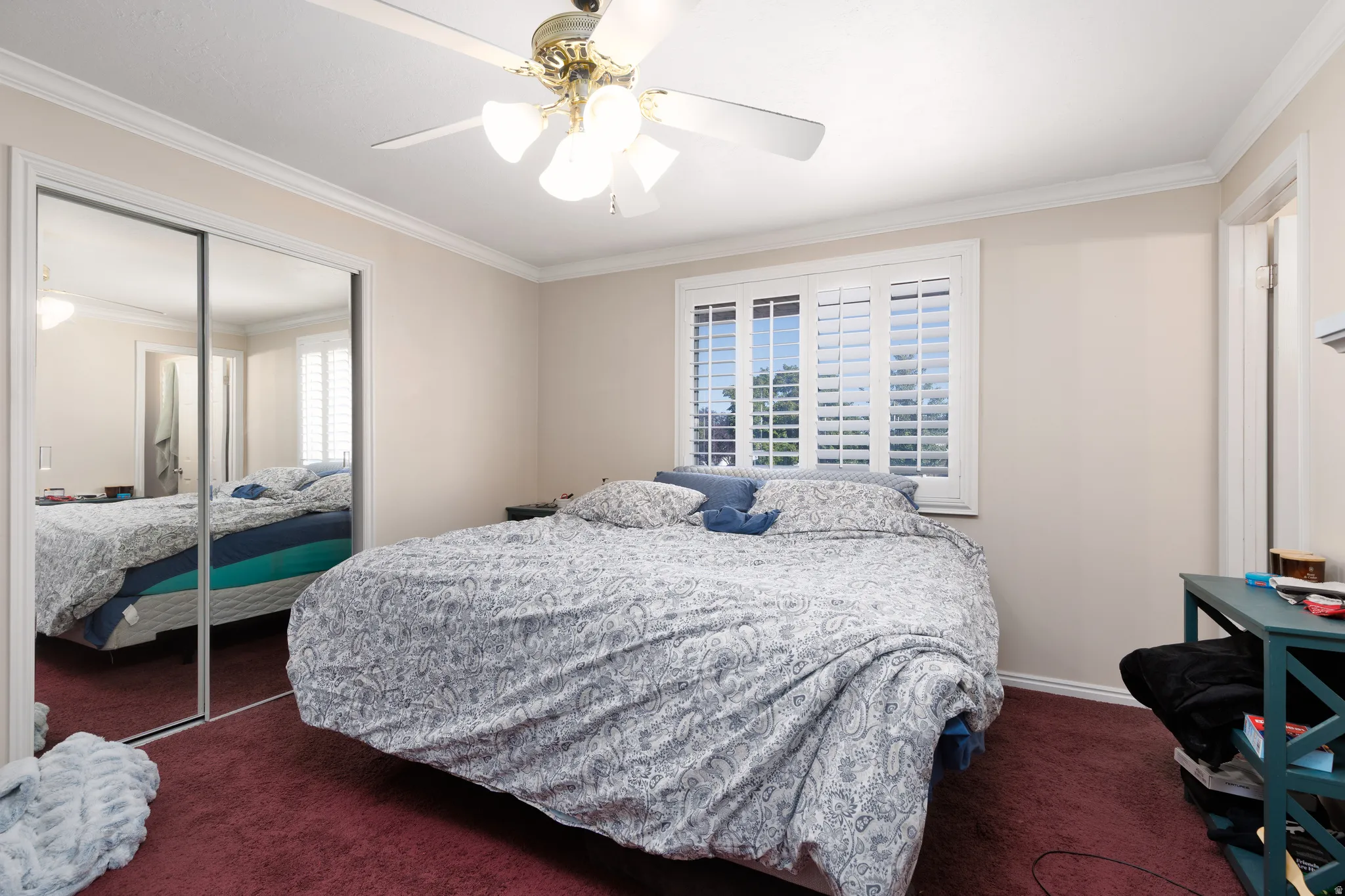Room featuring crown molding, a ceiling fan with integrated lighting, a window with plantation shutters, and a mirrored sliding closet door
