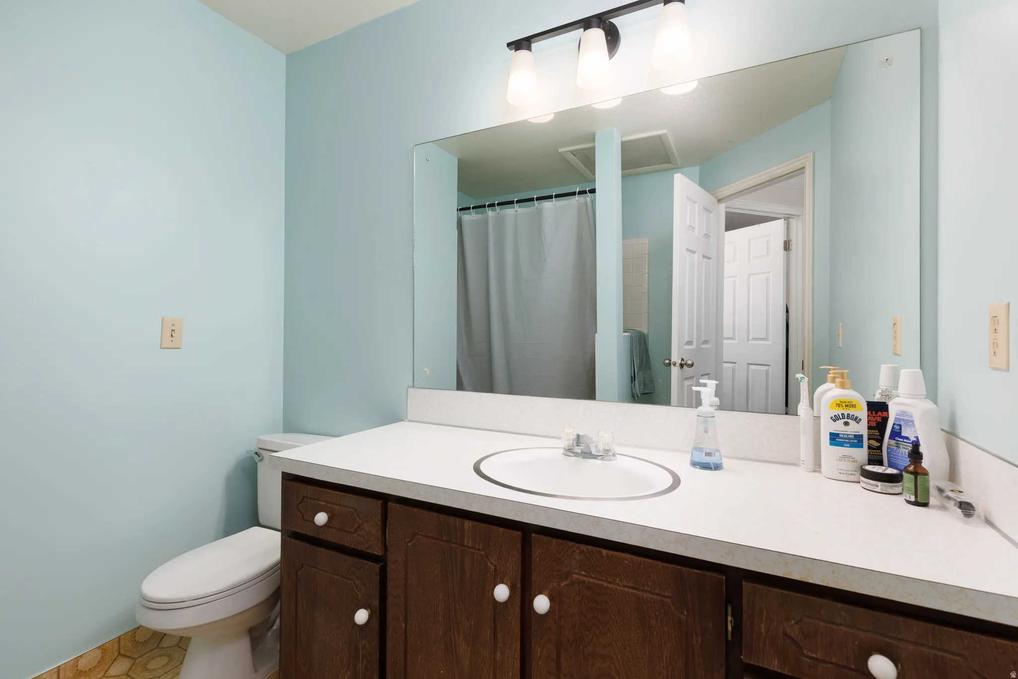 Full-width vanity mirror, dark wood-finish cabinetry, white countertop, integrated sink, and track lighting with frosted glass shades