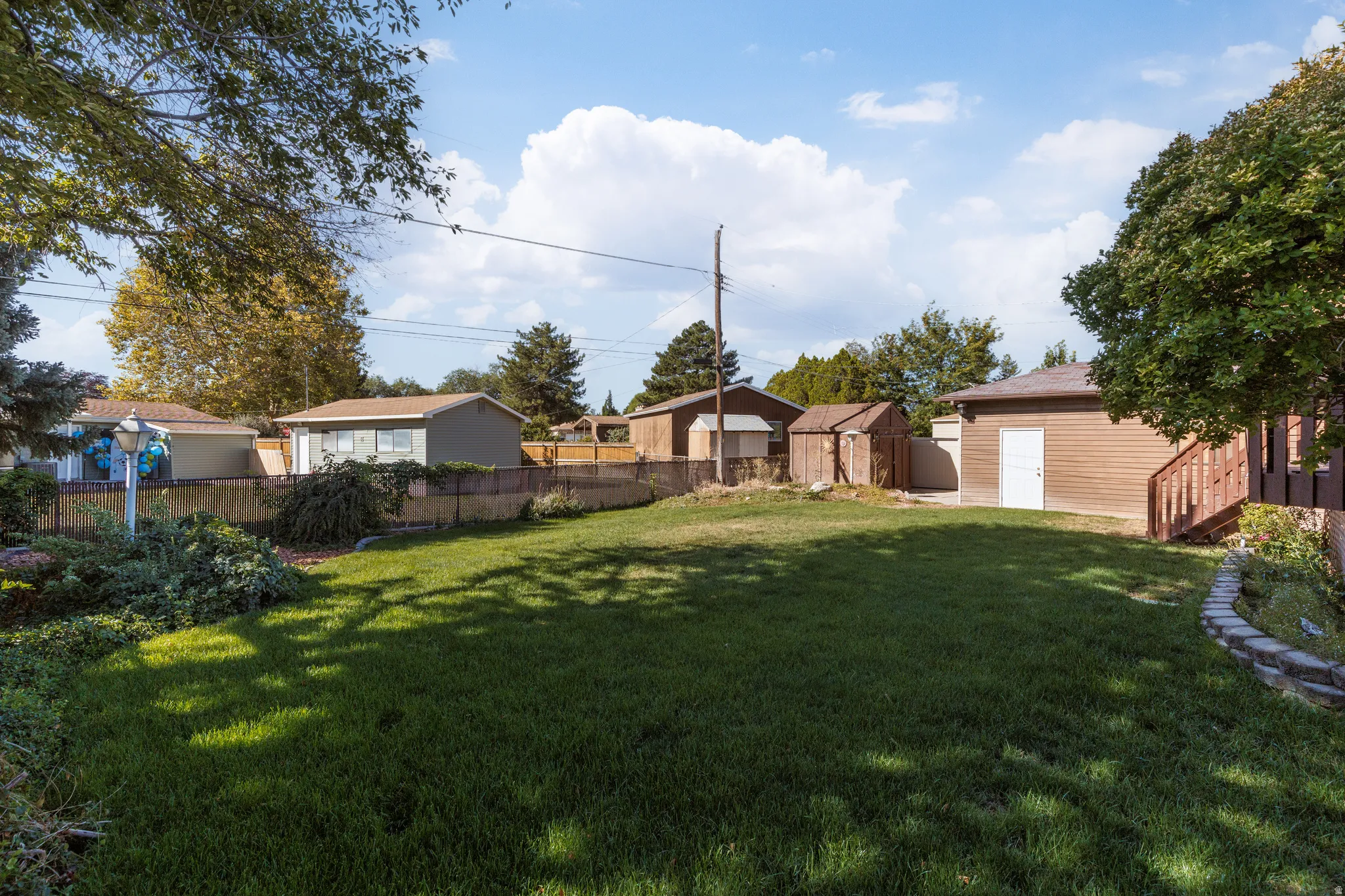 Expansive backyard featuring a manicured lawn, established trees, a wood-sided outbuilding with exterior stairs, and a privacy fence
