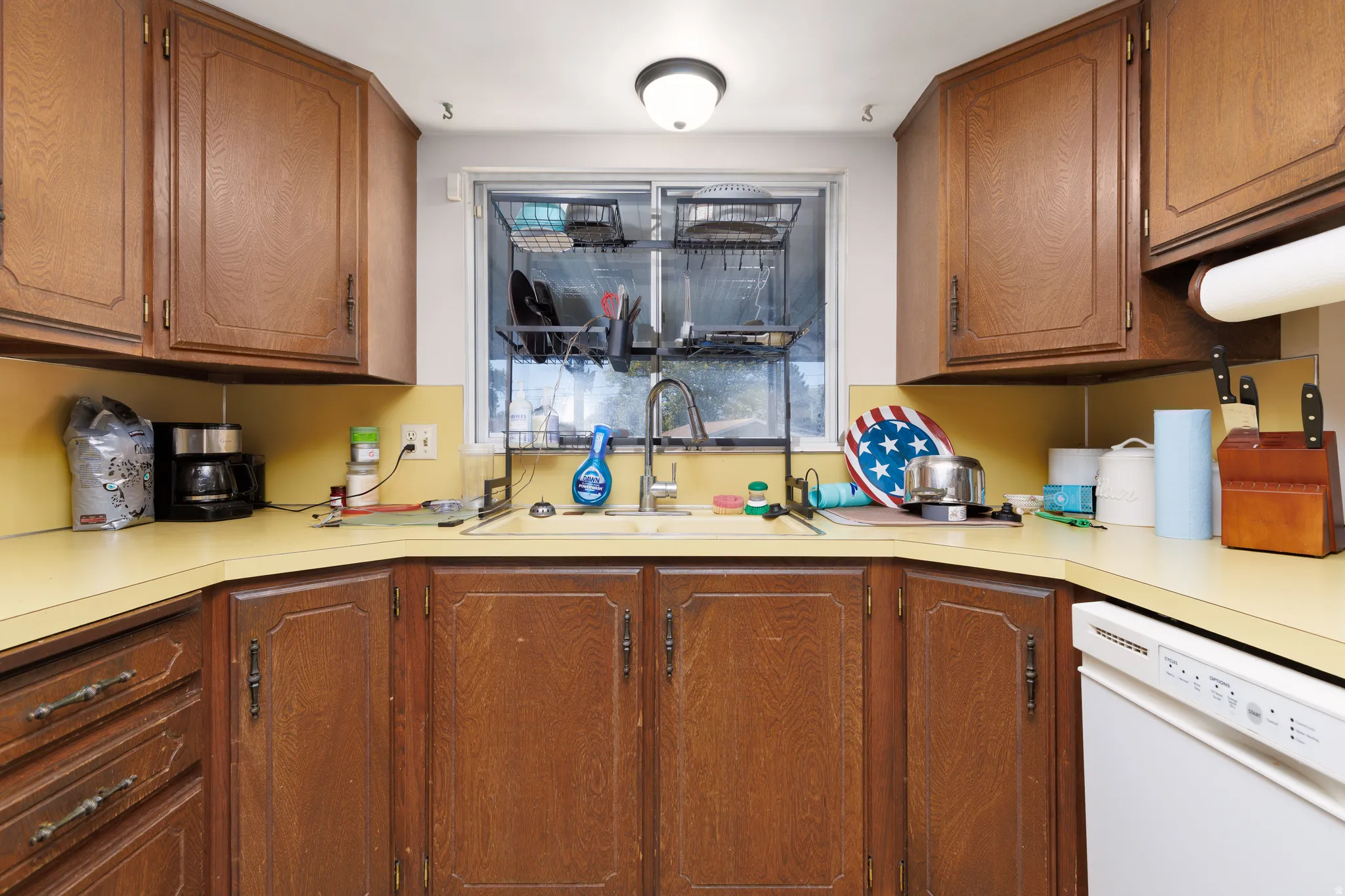 Kitchen featuring wood-finish cabinetry, a single basin sink, a window over the sink, and a dishwasher