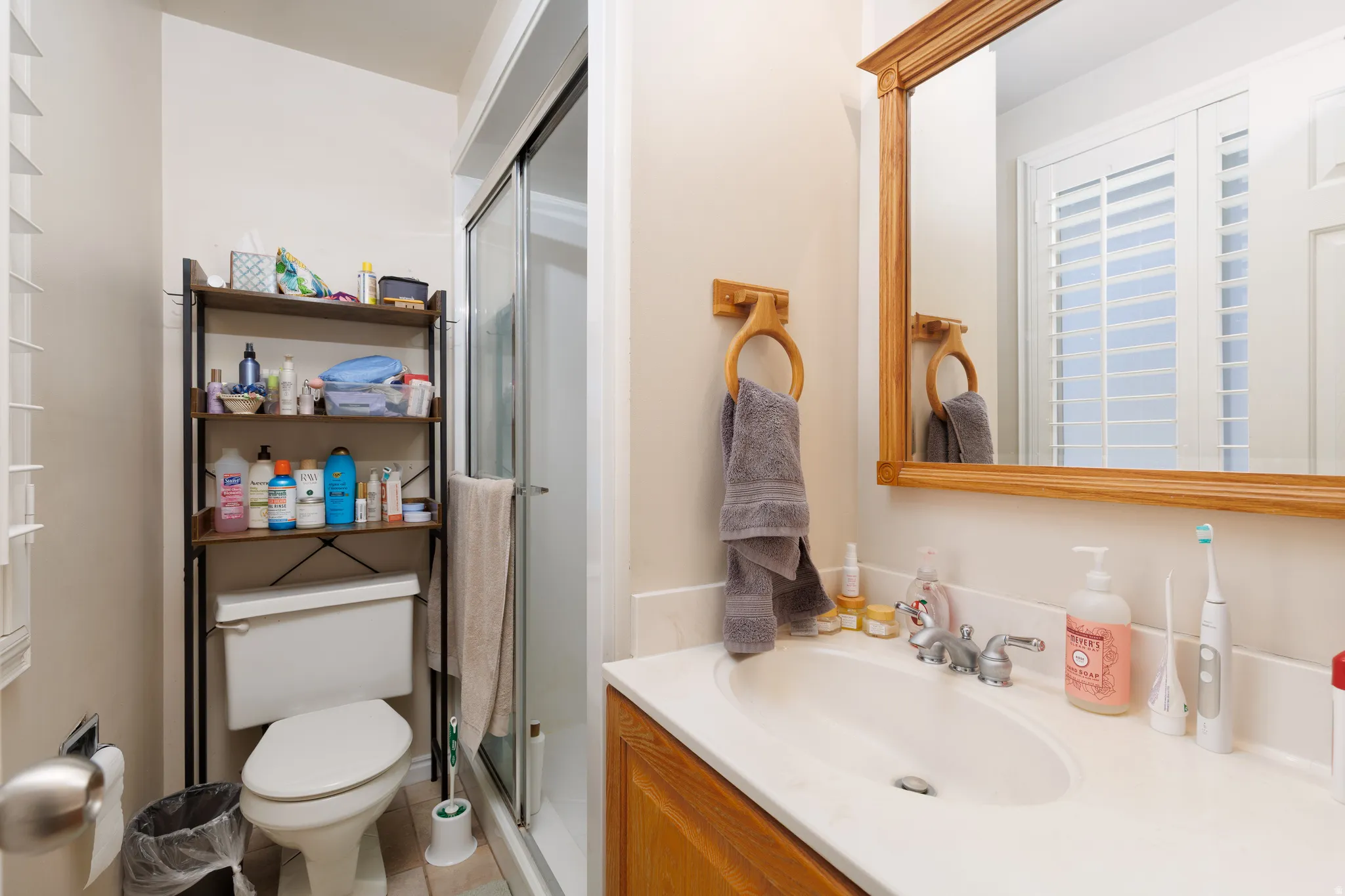 Bathroom featuring a single vanity with a laminate countertop, wood-finish cabinetry, a framed mirror, a toilet, and a glass-enclosed shower