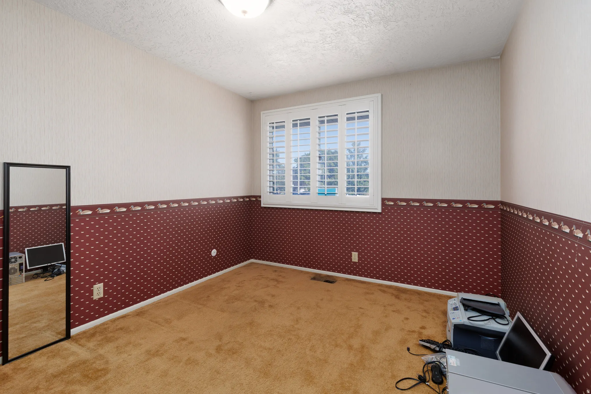Window with white plantation shutters, textured wall covering, and carpeted flooring