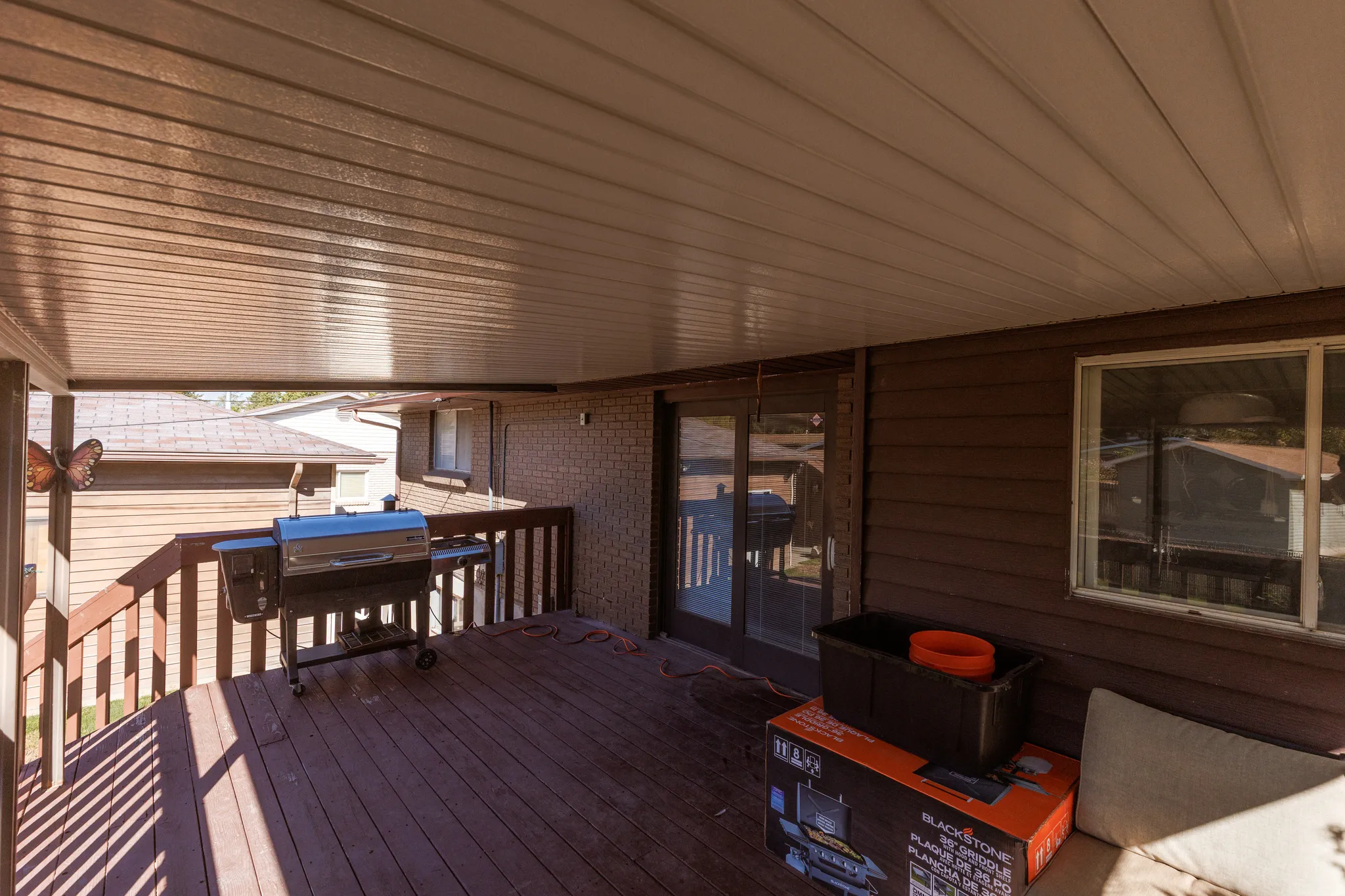 Covered wooden deck with wooden railings, dark siding, and a sliding glass door