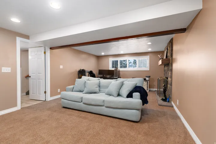 Carpeted living space featuring a stone-clad fireplace, recessed lighting, and a white plantation-shuttered window