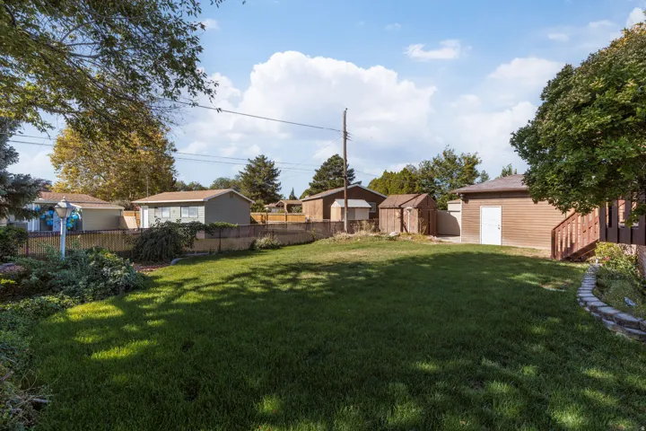 Expansive backyard featuring a manicured lawn, established trees, a wood-sided outbuilding with exterior stairs, and a privacy fence